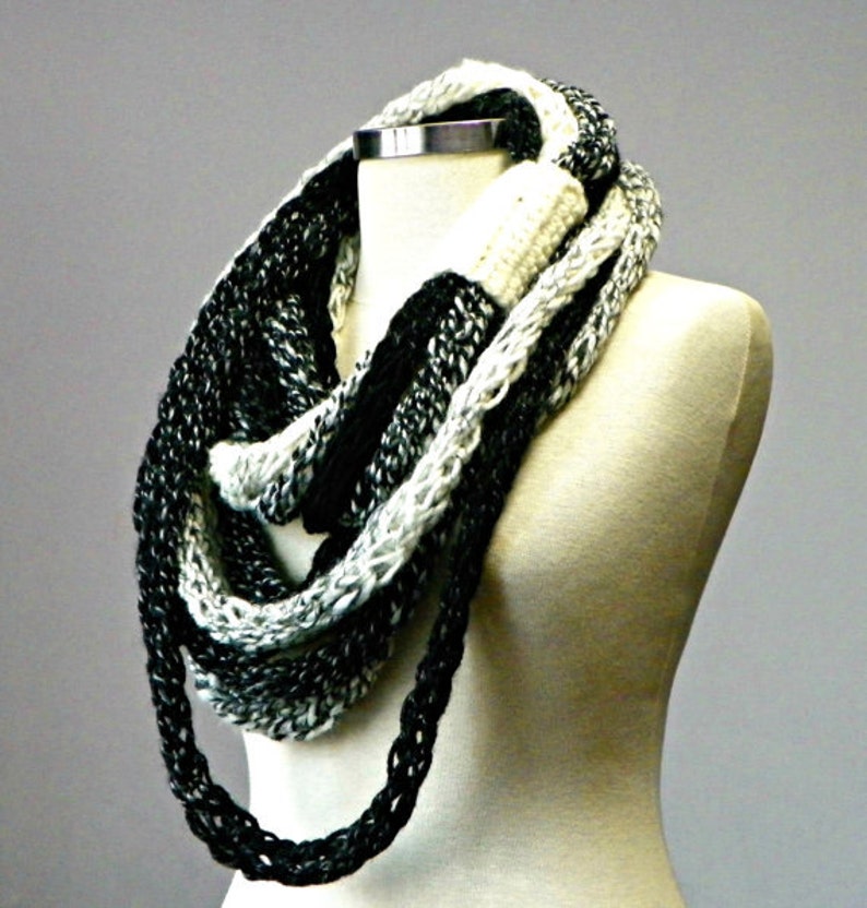 May include: A black and white infinity scarf made of chunky yarn. The scarf is looped around a white mannequin's neck.