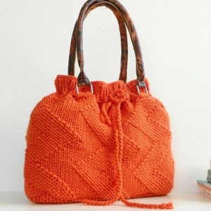 May include: Orange knitted tote bag with leather handles. The bag has a drawstring closure and a diamond pattern.