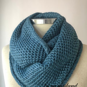 Peut inclure: Une écharpe en tricot bleu sarcelle, réalisée avec un point texturé. L'écharpe est présentée sur un mannequin.