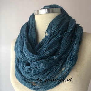 May include: A teal blue crocheted infinity scarf with a delicate openwork pattern. The scarf is displayed on a mannequin.