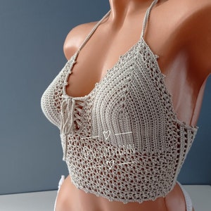 Pu&ograve; includere: Un top halter in crochet beige con un dettaglio di pizzo sul davanti. Il top &egrave; realizzato con un delicato motivo a punto aperto.