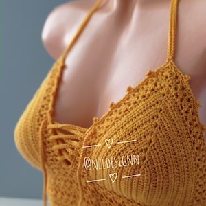 Pu&ograve; includere: Un top halter in crochet giallo senape con un dettaglio di pizzo sul davanti. Il top presenta un delicato motivo a crochet ed &egrave; realizzato con un filato morbido e leggero. Il testo "@NZLDESIGNN" &egrave; visibile sul top.