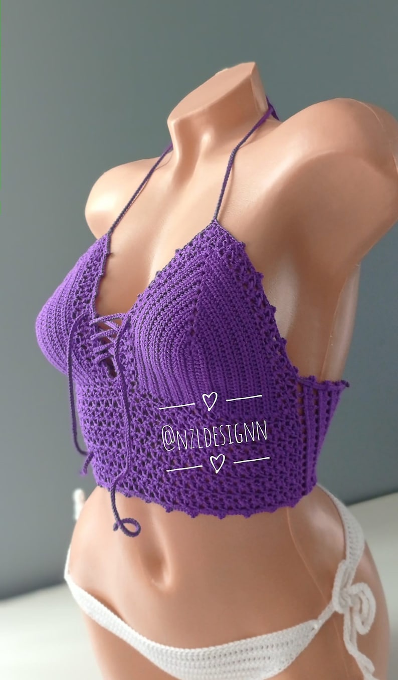 Pu&ograve; includere: Top halter in crochet viola con un laccio sul davanti. Il top &egrave; su un manichino e ha il testo "@NZLDESIGNN" su di esso.