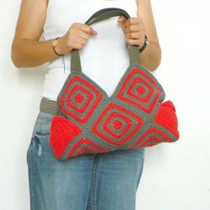 May include: A crocheted handbag with a gray and red geometric pattern. The bag has a leather strap and a large, open top.