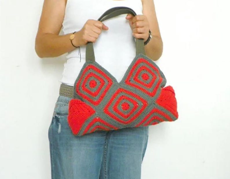 May include: A crocheted handbag with a gray and red geometric pattern. The bag has a leather strap and a large, open top.
