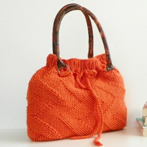 May include: Orange knitted tote bag with brown handles. The bag has a drawstring closure and a diamond pattern.