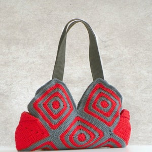 May include: A gray and red crocheted tote bag with a geometric pattern. The bag has two straps and a wide base.