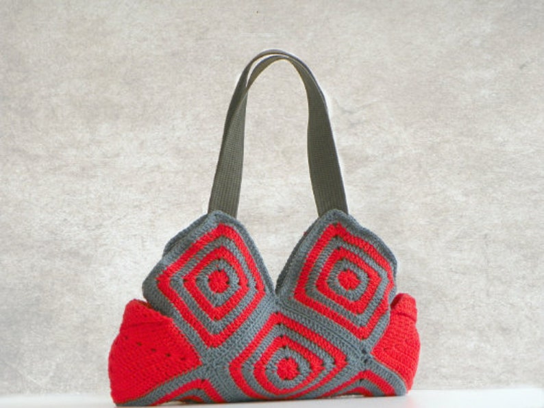 May include: A gray and red crocheted tote bag with a geometric pattern. The bag has two straps and a wide base.