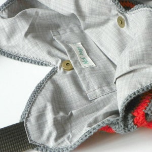 May include: A gray crocheted tote bag with a red and gray striped pattern. The bag has a zipper closure and a small pocket on the inside. The bag has a label that says "Nici Bags".