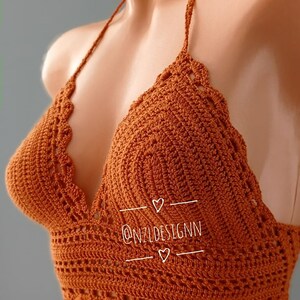 Pu&ograve; includere: Un top halter in crochet marrone con un bordo a festoni. Il top ha una scollatura a V ed &egrave; realizzato con un punto delicato. Il testo "@NZLDESIGNN" &egrave; visibile sul top.
