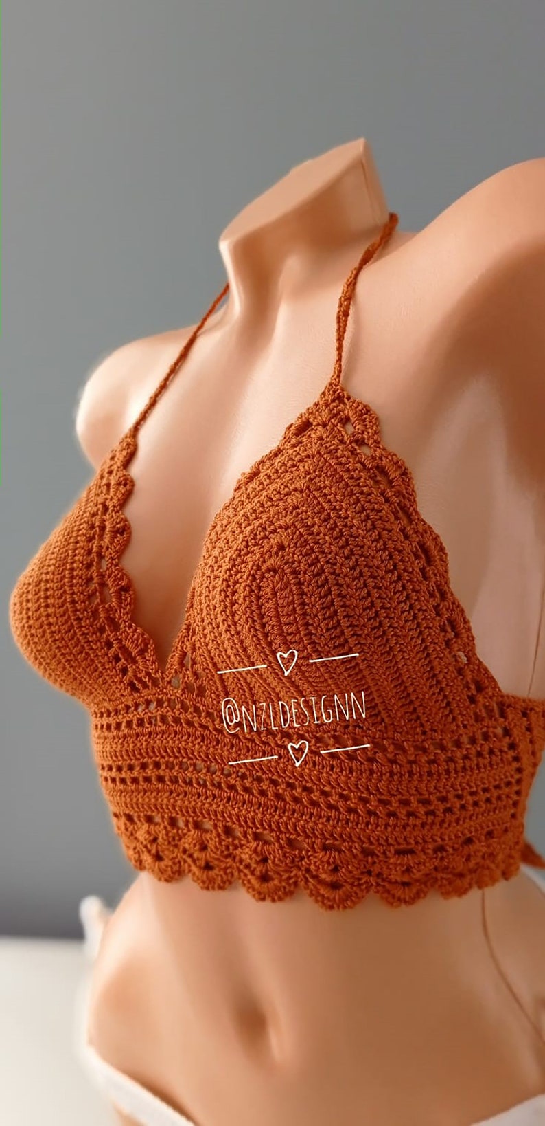 Pu&ograve; includere: Un top halter in crochet marrone con un bordo a festoni. Il top ha una scollatura a V ed &egrave; realizzato con un punto delicato. Il testo "@NZLDESIGNN" &egrave; visibile sul top.