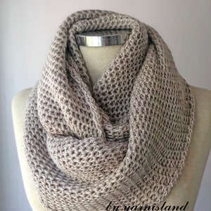 May include: A beige knitted infinity scarf with a textured pattern. The scarf is displayed on a white mannequin. The text "by yarnisland" is visible at the bottom of the image.