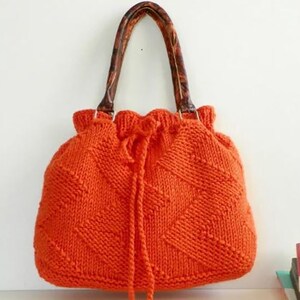 May include: A bright orange knitted tote bag with brown leather handles. The bag has a drawstring closure and a diamond pattern.