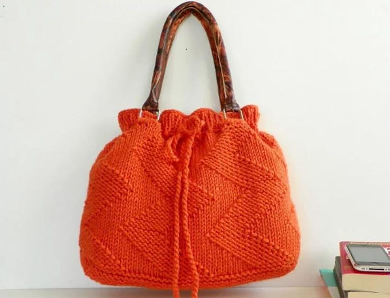 May include: A bright orange knitted tote bag with brown leather handles. The bag has a drawstring closure and a diamond pattern.