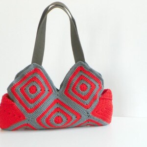 May include: A red and gray crocheted tote bag with two gray fabric straps. The bag is made of squares with a circular pattern.