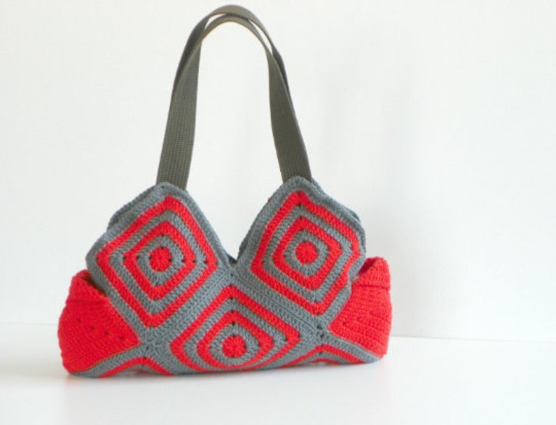 May include: A red and gray crocheted tote bag with two gray fabric straps. The bag is made of squares with a circular pattern.