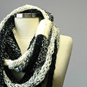May include: A black and white infinity scarf made of chunky yarn. The scarf is knit in a loose, open stitch.