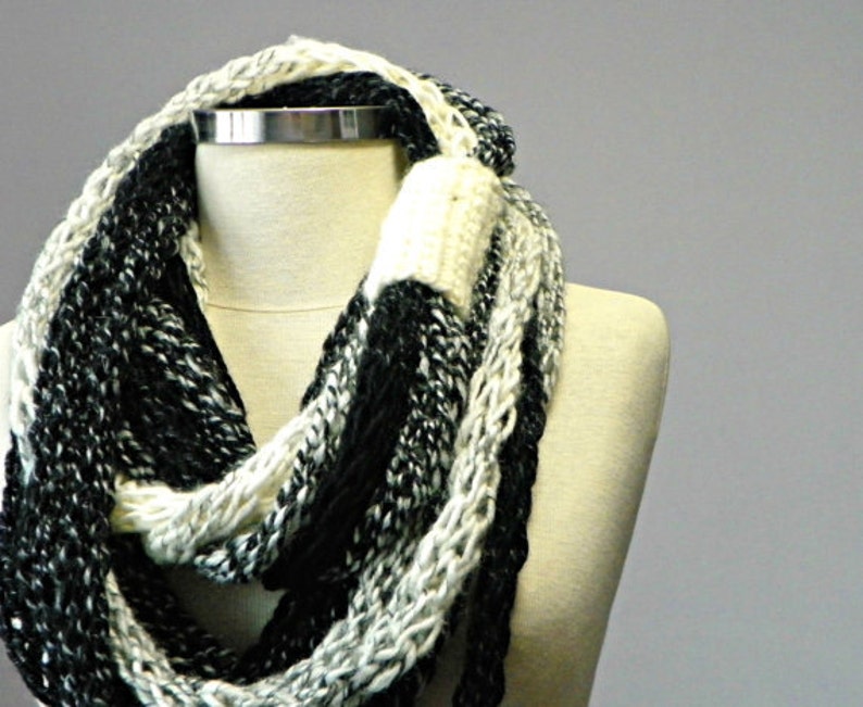 May include: A black and white infinity scarf made of chunky yarn. The scarf is knit in a loose, open stitch.