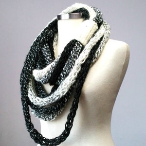 May include: A black and white infinity scarf made of knitted yarn. The scarf is draped over a white mannequin.