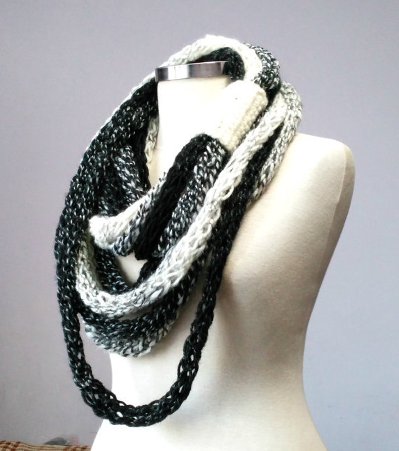May include: A black and white infinity scarf made of knitted yarn. The scarf is draped over a white mannequin.
