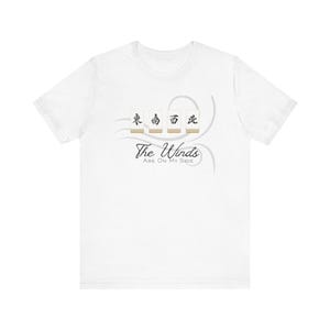 Op de afbeelding: Wit t-shirt met de tekst "The Winds Are On My Side" onder vier Mahjong-tegels met Chinese karakters. Het ontwerp bevat een grijs wervel-element.
