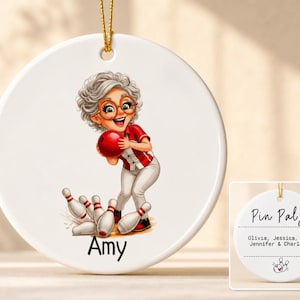 May include: A round white ceramic ornament featuring a cartoon illustration of a person with gray hair and glasses holding a red bowling ball, with bowling pins at their feet and the name Amy printed below. The reverse side displays the text Pin Pals.