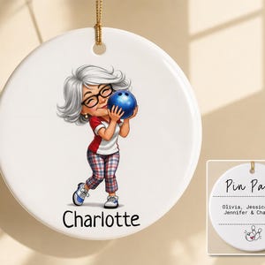 May include: A round white ceramic ornament featuring a cartoon illustration of a person with gray hair and glasses holding a blue bowling ball. The name Charlotte is printed below the figure. The reverse side displays the text Pin Pals with the names Olivia, Jessica, Amy, Jennifer, and Charlotte, plus a small bowling pin graphic.