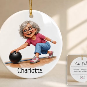 May include: A round white ceramic ornament featuring a cartoon illustration of a gray-haired person in a pink shirt and blue pants bowling with a black ball. The name Charlotte is printed below. The reverse side displays the text Pin Pals and names.