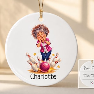May include: A round white ceramic ornament featuring a cartoon illustration of a person with curly hair wearing a pink shirt and blue pants, surrounded by bowling pins and a ball. The name Charlotte is printed below, with a gold hanging cord.