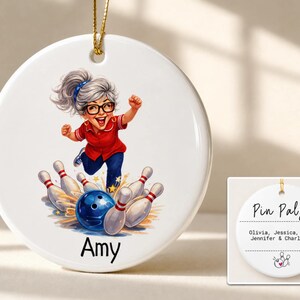 May include: A round white ceramic ornament featuring a cartoon illustration of a person with gray hair in a ponytail, wearing glasses and a red shirt, bowling with a blue ball and white pins. The name Amy is printed below. The reverse side says Pin Pals.