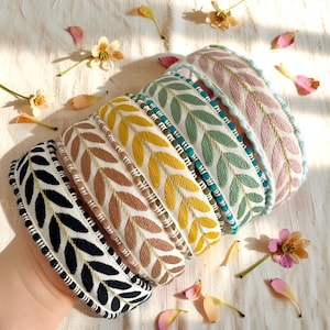 Peut inclure: Plusieurs bandeaux pour cheveux ornés de motifs de feuilles brodées. Les bandeaux présentent diverses couleurs, notamment le noir, le marron, le jaune, le vert et le rose. Chaque bandeau a un motif de feuilles unique et une bordure contrastante.