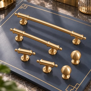 May include: A collection of brushed gold cabinet hardware including two long bar pulls with decorative end caps, two smaller T-bar handles, and two spherical knobs. Each piece features a smooth metallic finish and a sturdy mounting base.