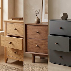 May include: A triptych of wooden dressers in varying shades. The first is light oak with a drawer open, the second is walnut, and the third is a dark gray. Each has round, dark knobs. The dressers are set against a neutral background.