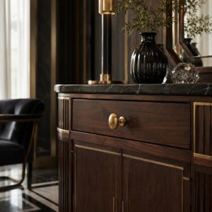 May include: A dark wood cabinet featuring a single drawer with a round brass knob, two lower doors with vertical paneling, and a black marble top. The piece is accented with thin brass trim along the edges and vertical side detailing.