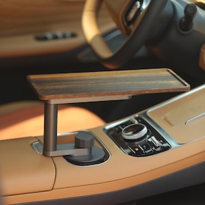 Op de afbeelding: Een houten autotray met een donkere afwerking, gemonteerd op een metalen steun. De tray is gepositioneerd boven de middenconsole van een auto met een tan lederen interieur en een zwart stuurwiel.