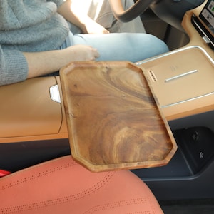 Puede incluir: Una bandeja rectangular de madera con un patrón de vetas naturales. La bandeja tiene forma octogonal y está colocada en un coche. El interior del coche es de color beige y gris.
