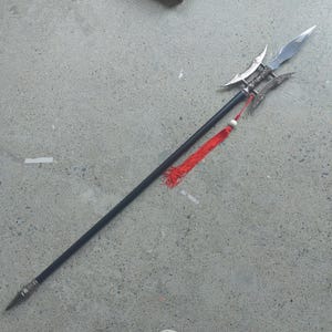 May include: A black spear with a silver blade and decorative elements. The spear features a red tassel and a pointed tip. The weapon is designed with a long, black shaft and ornate metalwork.