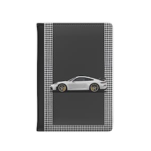 May include: A white sports car with gold wheels is featured on a notebook cover. The cover has a black and white checkered pattern border and a solid black background. The notebook's spine is black.
