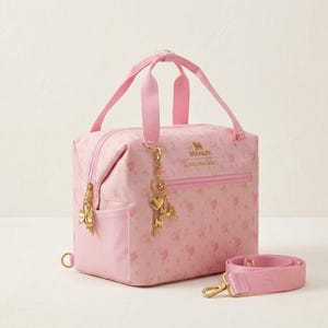 May include: A pink floral Stanley bag with a top handle and a detachable shoulder strap. The bag features gold-colored hardware, including a zipper, charms, and a clasp. The text "STANLEY LOVEISRADIANCE" is printed on the front.