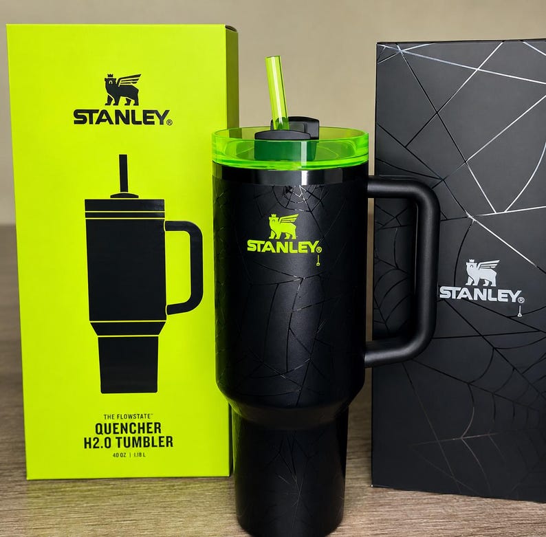 May include: Black Stanley Quencher H2.0 tumbler with a green lid and straw. The tumbler has a handle and is next to a bright green box and a black box. The tumbler is 1.18L.