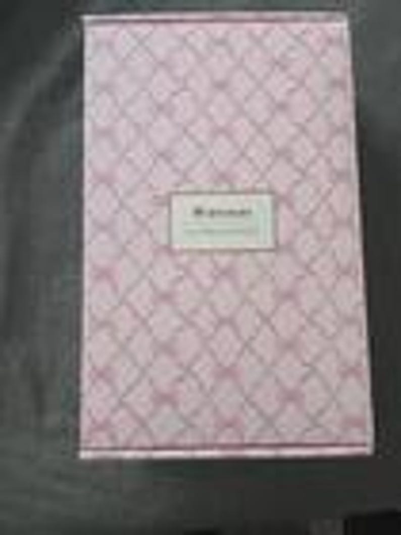 May include: A rectangular pink box with a diamond pattern and a white label in the center. The label has the text "My Journal" in a serif font. The box is closed and appears to be made of cardboard.