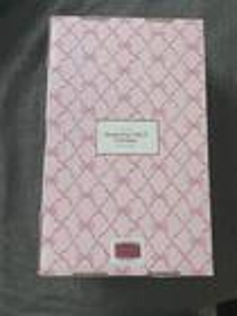 May include: A pink and white patterned box with the text "Something Nice" in a rectangular label. The box has a diamond pattern and a small rectangular label at the bottom. The box is closed.