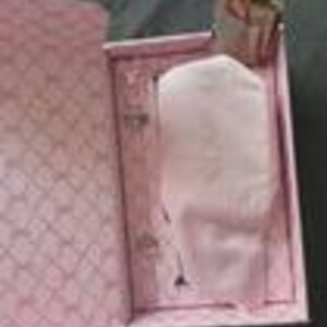 May include: A pink gift box with a diamond pattern on the inside and a white object wrapped in pink tissue paper. The box is open, revealing the contents. The background is a dark gray surface.