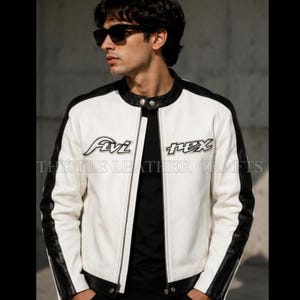 May include: White leather jacket with black accents on the shoulders and sleeves. The jacket has a zipper closure and a round collar. The text "Avi Rex" and "THISTLE LEATHER CRAFTS" are embroidered on the front.