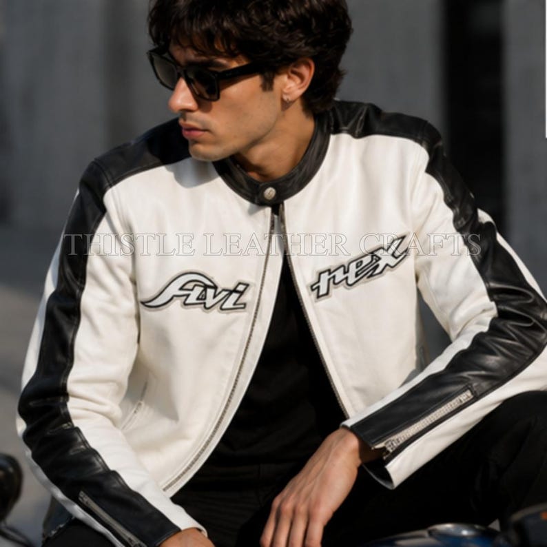 May include: A white and black leather jacket with the text "Avi Rex" on the front. The jacket has black sleeves and a black collar. The jacket is zipped up and has a classic motorcycle jacket design.