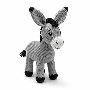 Puede incluir: Un juguete de burro tejido a mano en tonos grises, negros y blancos. El burro tiene orejas largas, una melena negra y una cola pequeña. Está de pie sobre cuatro patas con pezuñas negras. Un adorable peluche.