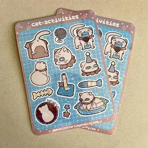 May include: Two sticker sheets with cat-themed illustrations. Each sticker features a cat in various activities, such as playing with yarn, wearing a party hat, and drinking from a wine glass. The stickers have a blue grid background with the text "cat-activities".