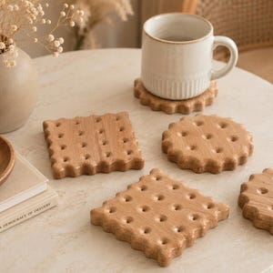 May include: A collection of wooden biscuit-shaped coasters, each with a wavy edge and small holes. A white mug rests on one coaster. The coasters are displayed on a light-coloured surface, suitable for a kitchen or dining area.