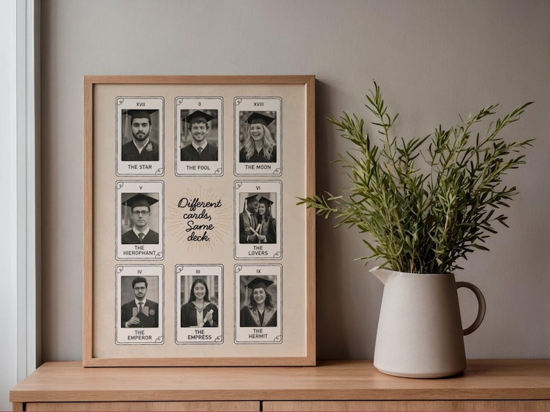 May include: A wooden framed print displaying black and white photographs of people in graduation gowns, styled as tarot cards. The text "Different cards, Same deck" is in the center. A vase with greenery sits on a wooden surface.