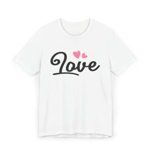 Peut inclure: T-shirt blanc avec le mot "Love" en écriture noire cursive, accompagné de deux cœurs roses. Le t-shirt a un col rond et des manches courtes, parfait pour un usage quotidien.